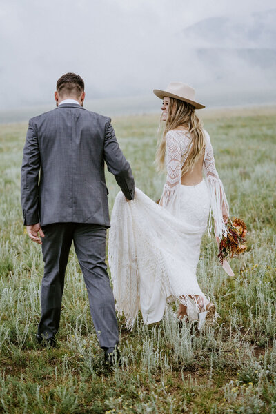 bride and groom holding hands walking in field