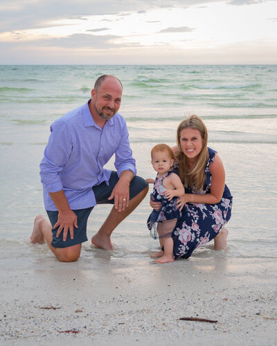 a man and woman posing on the beach with a baby wearing blue and purple clothing