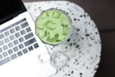 Matcha latte sitting on marble table with computer and head phones