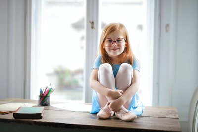 red-headed elementary student sitting in homeschool windowseat wearing blue dress
