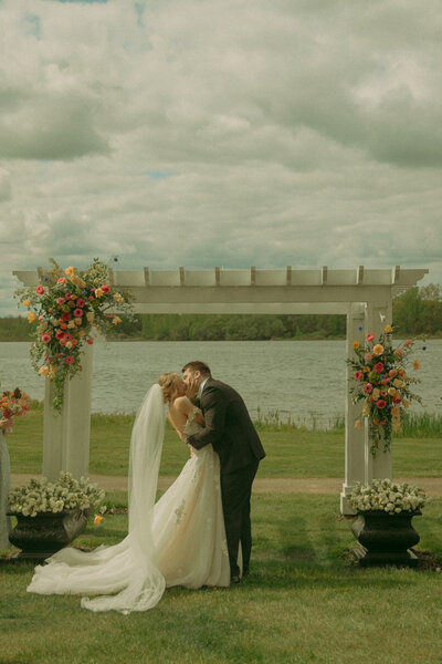 A bride and groom walk hand in hand along the sandy beach at dusk 