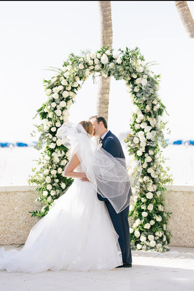 Wedding couple at the Ritz Carlton Sarasota in front of a floral arch at their ceremony by Angelika Krug Photo & Film