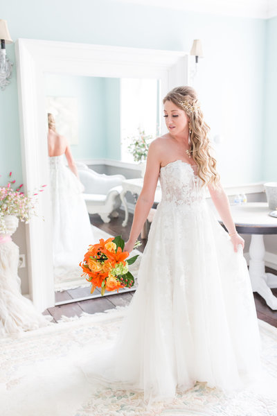Beautiful bride poses in her wedding gown while holding orange and yellow bouquet