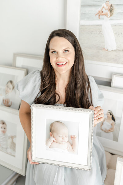 Connecticut family photographer, Kristin Wood, smiles while holding framed portrait of a newborn