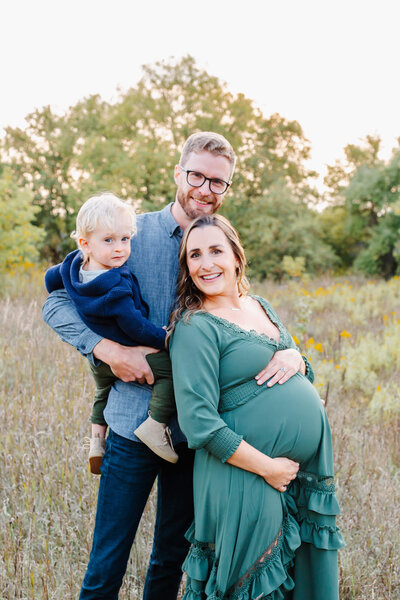 woman in green dress hold her belly in a beautiful field as she wears a Baltic Born dress