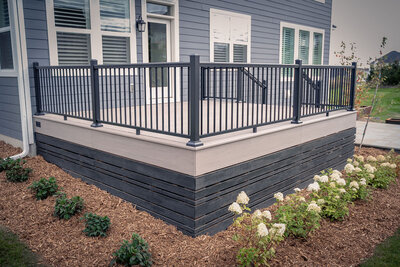 A low PVC deck with aluminum railing and dark skirting around the base surrounded by fresh landscaping mulch and small shrubs. 