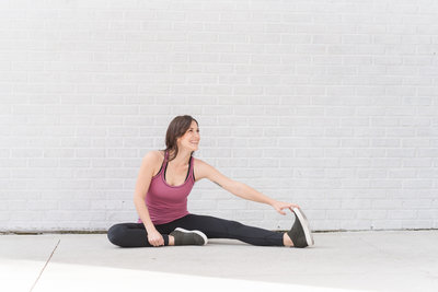 Fitness instructor stretches and smiles in front of white brick wall during branding photography session