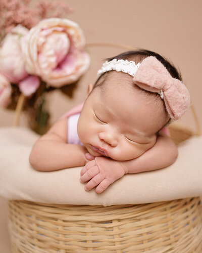 baby girl sleeping inside a basket of pink flowers
