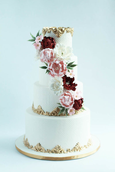 four tier white wedding cake with flowers and gold borders
