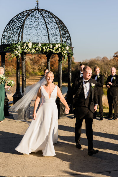 Couple smile at guests as they walk down the aisle.