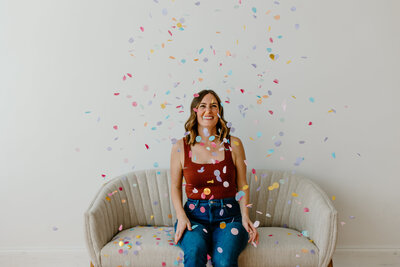 Bridget sitting on a vintage couch with colorful confetti falling all around her
