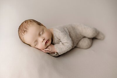 Charlotte baby lays on his side wearing a brown knit outfit with both hands underneath his cheek
