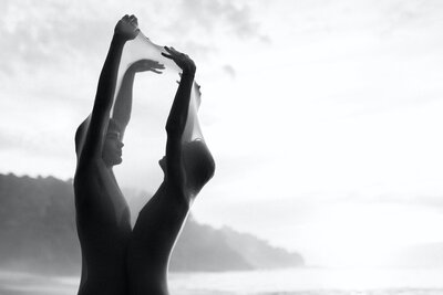 Black and white artistic destination couple photography of LGBTQ couple posing on a Mexican cliffside beach in the nude.