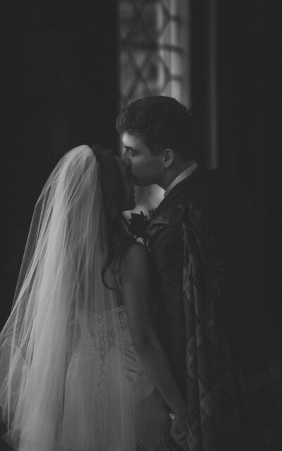 Black and white photo of a couple sharing a kiss inside St. Kirk Church, Scotland, capturing a timeless, intimate moment filled with love and emotion