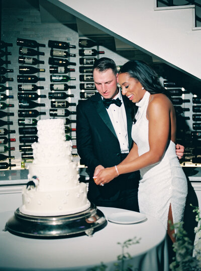 Bride and groom cutting 4-tiered cake during wedding reception at Knotting Hill Place