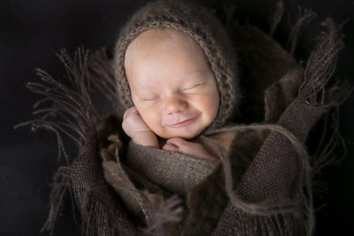 Sleeping newborn infant cuddled up with hat in Denver studio