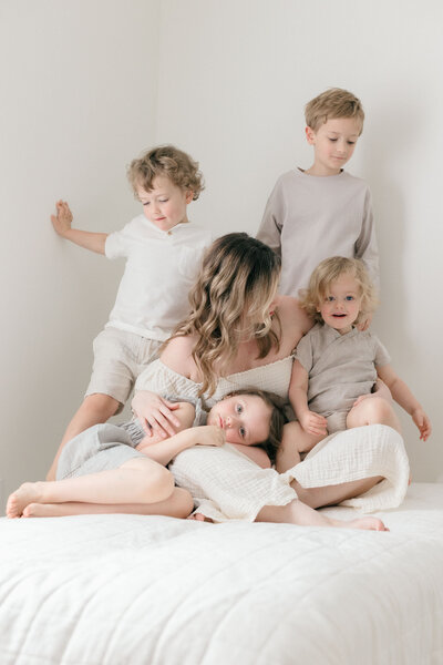 A photographer with her children all cuddling on a bed in all white studio