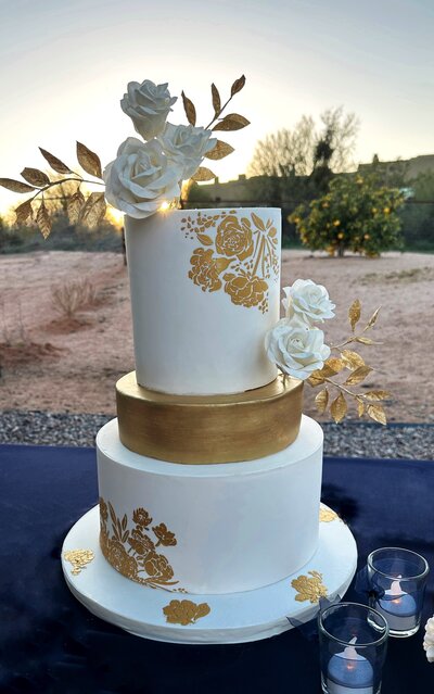 Gold and white 3 tier wedding cake with white sugar roses and gold leaves