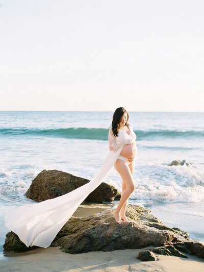 A pregnant mother to be looks down at her belly on hthe beach in Santa Barbara during her materntiy session