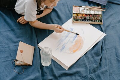 middle school girl laying on belly painting homeschool art