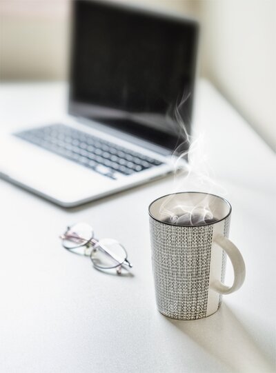 coffee cup next to a pair of glasses and a laptop