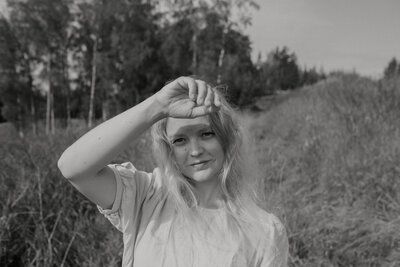 Henkilökuva naisesta, joka katsoo kameraan ja varjostaa silmiään kädellä maaseudulla kesällä Suomessa