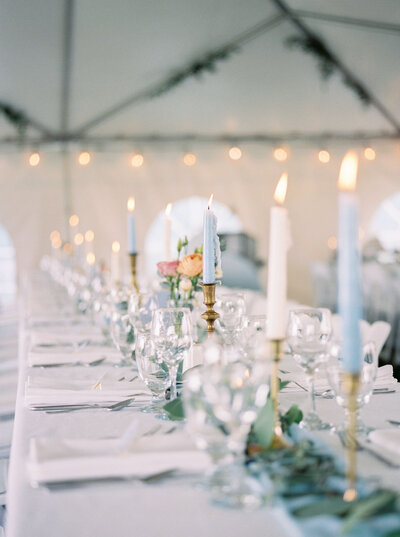 Wedding reception tablescape with blue and ivory taper candles, glasses and white napkins