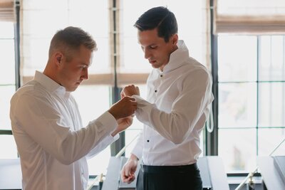 groomsman helping groom with shirt buttons