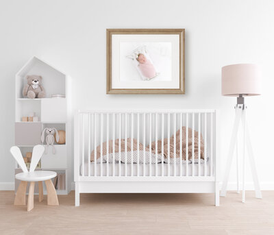 A newborn baby photograph printed and in a wooden frame hanging above a crib in a nursery