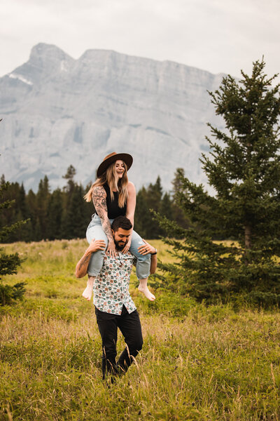 playful couple piggyback for candid image captured by Calgary wedding photographer