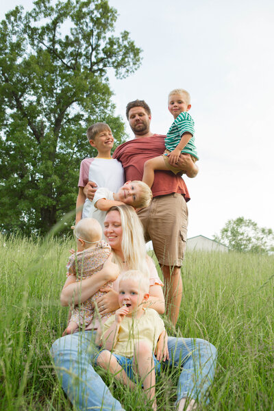 Family of five playing and laughing in a bright summer field, capturing genuine emotion and intimate, real-life moments.