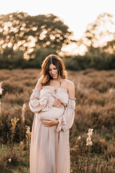 Photo of a pregnant woman standing in the sunset holding her bump