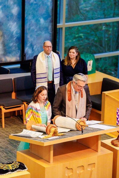A rabbi reads from the torah with a teen girl