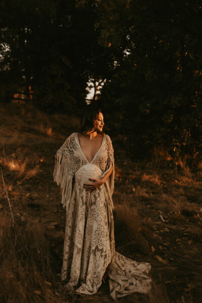 Expecting mother in a gorgeous reclamation dress facing toward the setting sun.