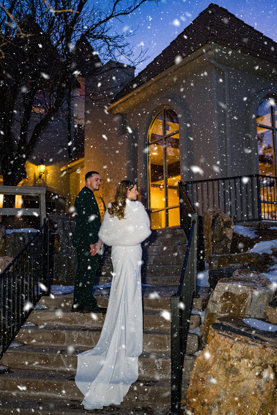 Bride and groom standing under snowfall at night during their winter wedding at Wedgewood Weddings in Colorado.