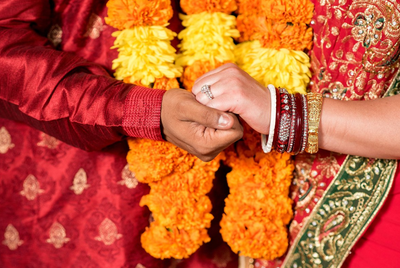 Detail of bride and groom holding hands with  Jaimala in the background