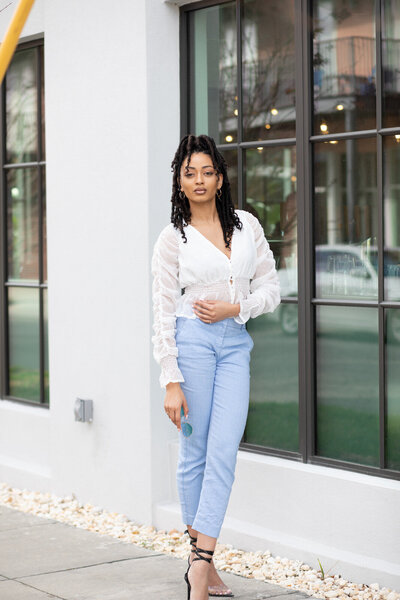african american woman in white shirt and blue jeans standing in front of window