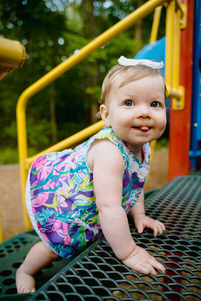 A baby smiling and climbing up playground stairs.