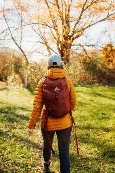 Meredith hiking in rhode island wearing a red backpack and yellow puffer jacket