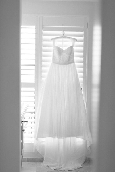 Light and airy wedding dress hanging on window shutters at wedding venue