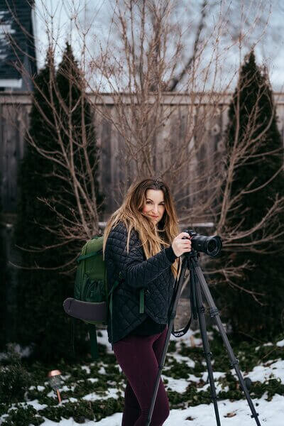 Gina sets up a tripod outdoors on a snowy day, likely preparing for a photoshoot in the crisp weather.