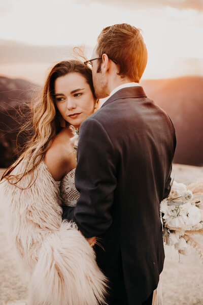 A bride and groom holding each other in front of a sunset