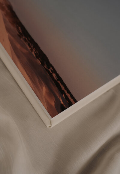 White leather wedding album open with evening landscape photo on top of  cream colored linen drape- Romero Album Design