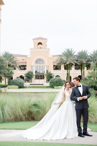 Photo of a wedding couple at the four seasons orlando with a view of the hotel in the background and the bride's long veil by Florida wedding photographer Angelika Krug Photo & Film. 