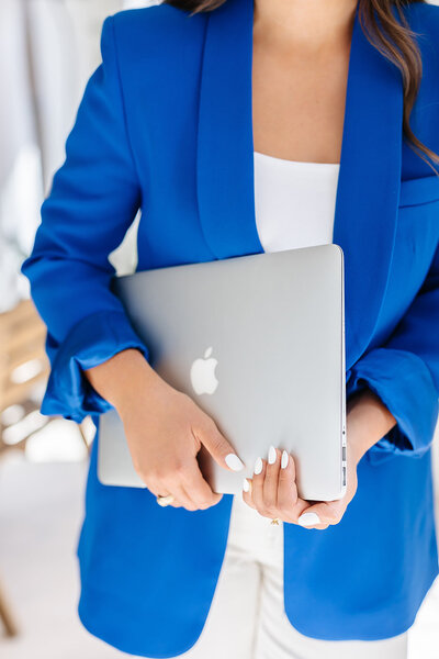 Abby Manawes in a bright blue blazer holding a laptop