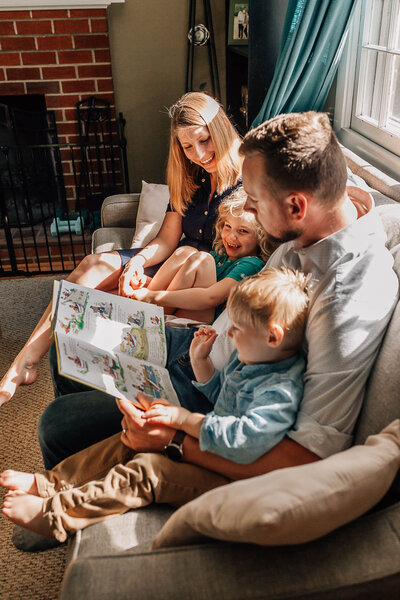 family of four sitting on the couch in their living room reading children's books together and  laughing captured by Hampton Roads best family photographer