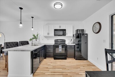Stylish black and white kitchen featuring modern appliances, pendant lighting, and wood flooring.