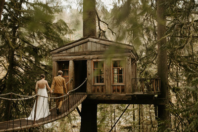 Couple walking across bridge to tree house in wedding attire