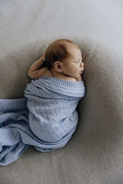 A newborn baby wrapped in a blue blanket taken by photographer Ada and Ivy