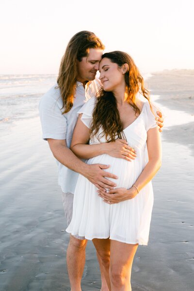 Couple embracing each other on beach with hands on baby bump